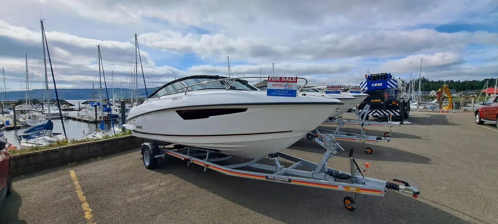 White speedboat on a trailer at a marina, marked "FOR SALE" with contact details for Approved Boats visible.
